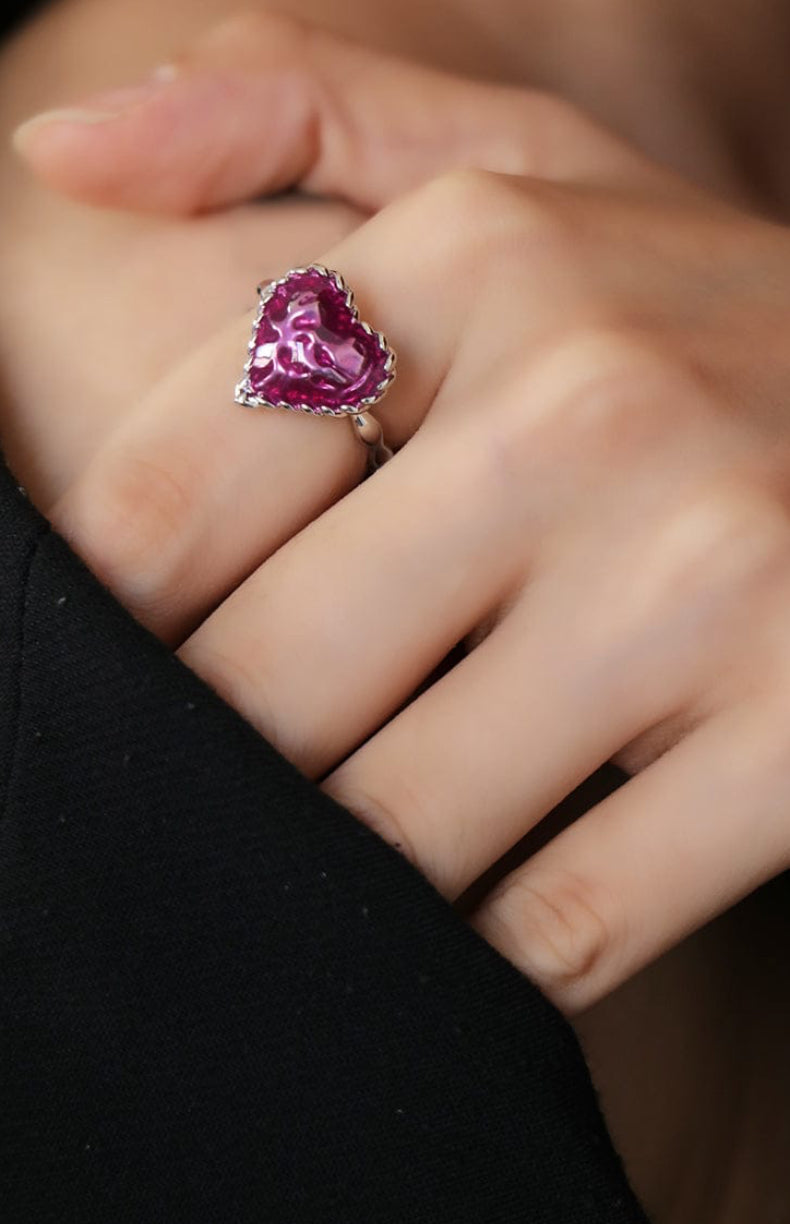 Hand wearing a ring with a pink gemstone on a blurred background