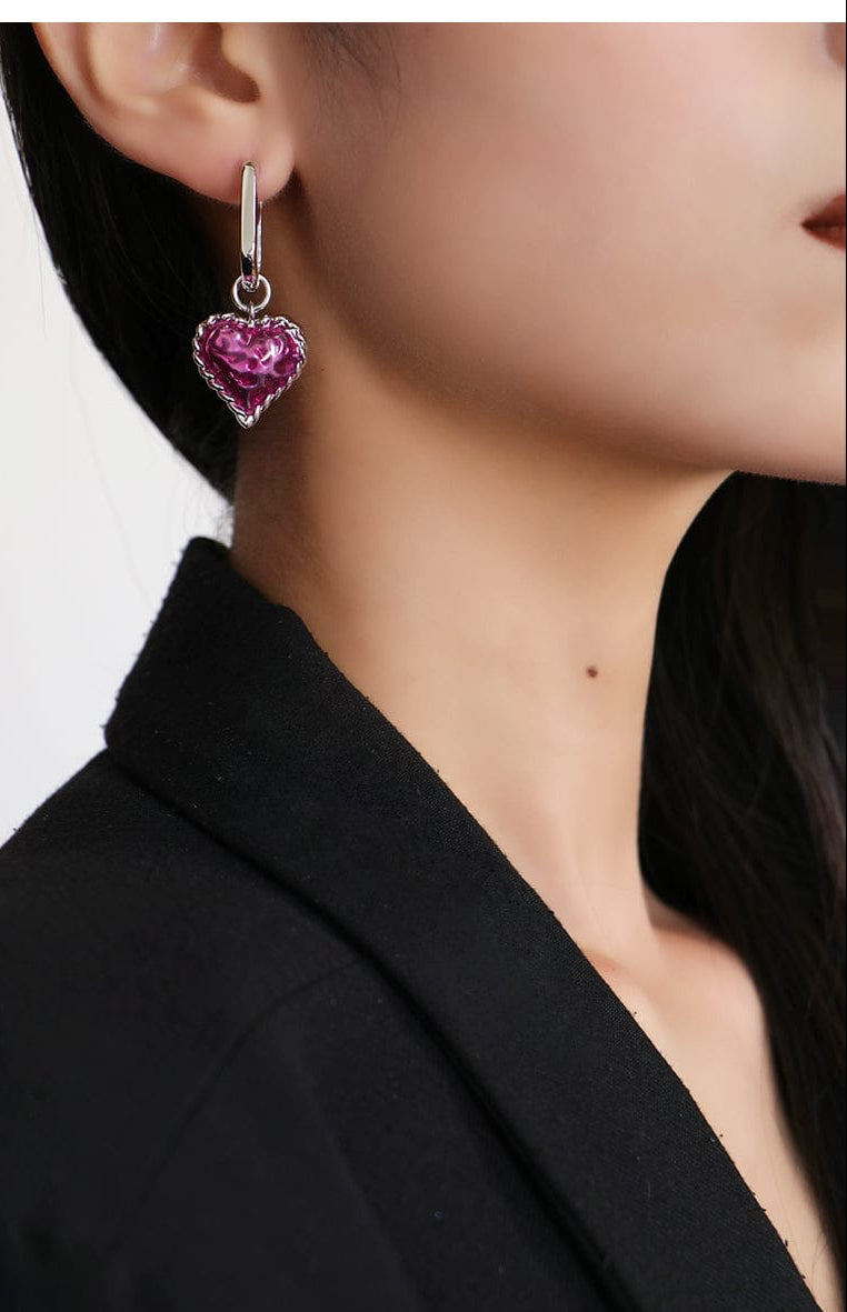 Close-up of a person wearing a heart-shaped pink earring with a black background