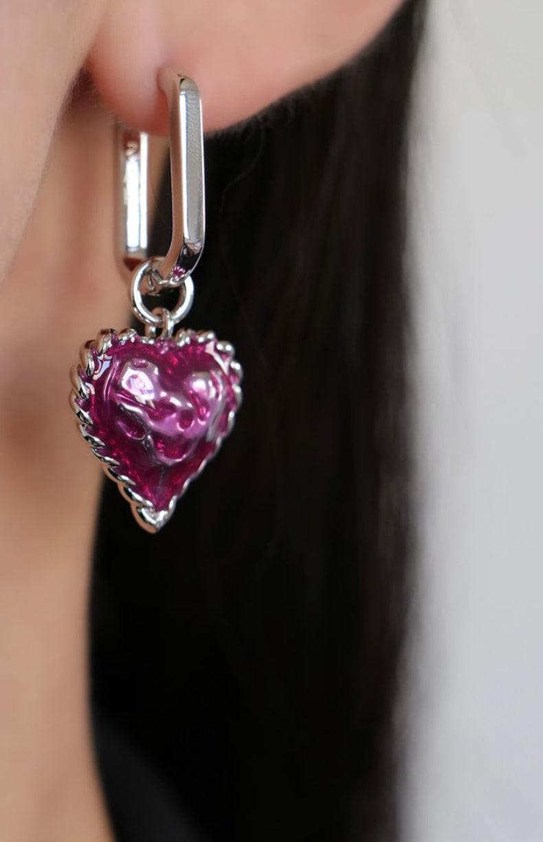 Silver earring with a pink heart-shaped charm worn by a person.