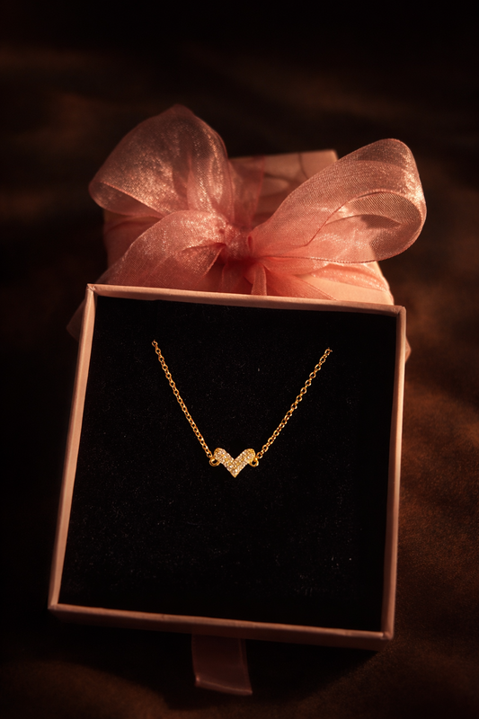 Gold necklace in a jewelry box with a pink bow on a dark background